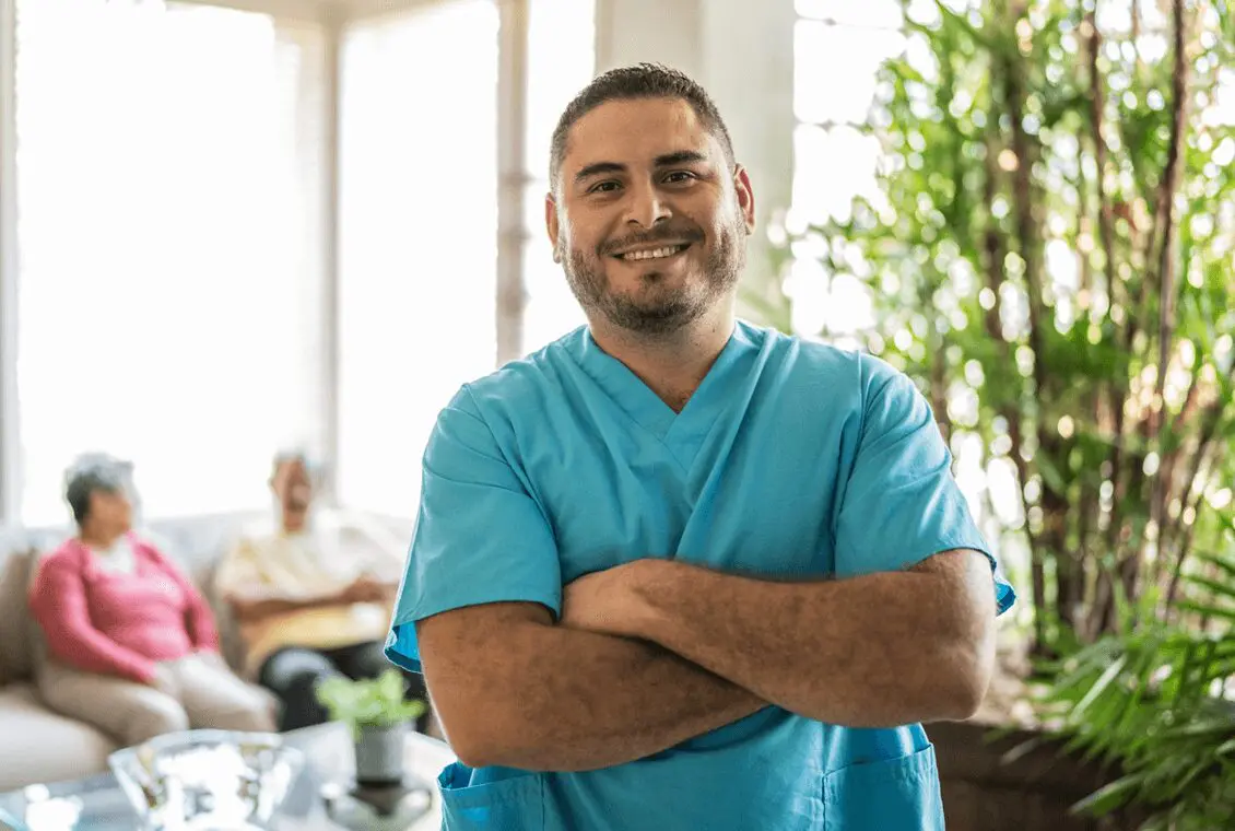 Smiling nurse in blue scrubs, arms crossed.